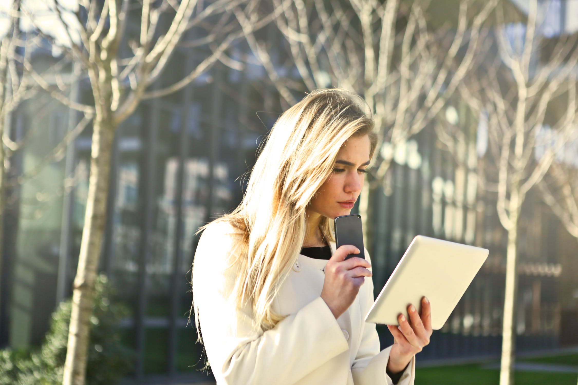 blonde female looking concerned at her teblet and holding her phone